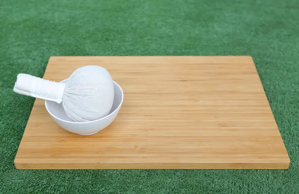 Bola de compresión a base de hierbas con flor de vela para el tratamiento de spa en tablero de madera de bambú contra el fondo de hierba — Foto de Stock