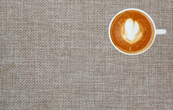 Vista superior de un café con patrón de corazón en una taza blanca sobre fondo de saco con espacio, arte latte — Foto de Stock
