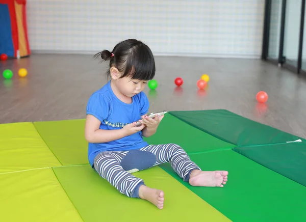 Primer plano lindo asiático bebé niña edad alrededor de un año de edad y nueve meses jugando un teléfono inteligente en el Kid habitación — Foto de Stock