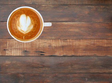 Kalp desenli beyaz bir fincan kahve üstten görünüm ahşap tahta arka plan, latte sanat üzerinde