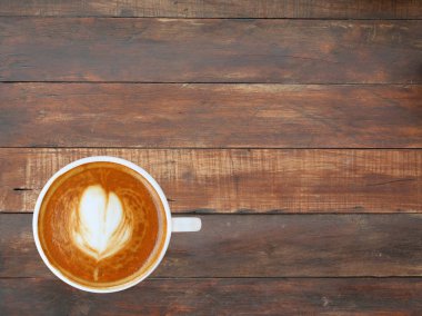 Kalp desenli beyaz bir fincan kahve üstten görünüm ahşap tahta arka plan, latte sanat üzerinde