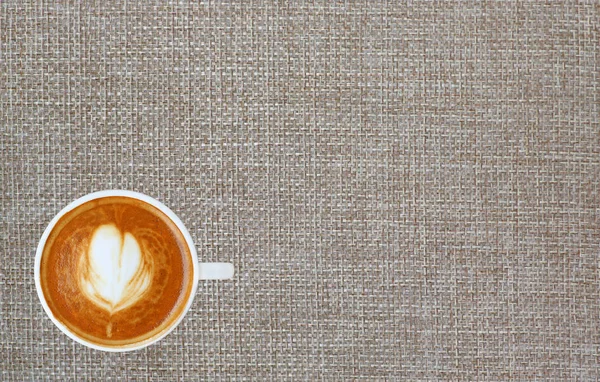 Vista superior de um café com padrão de coração em uma xícara branca no fundo saco com espaço, arte latte — Fotografia de Stock