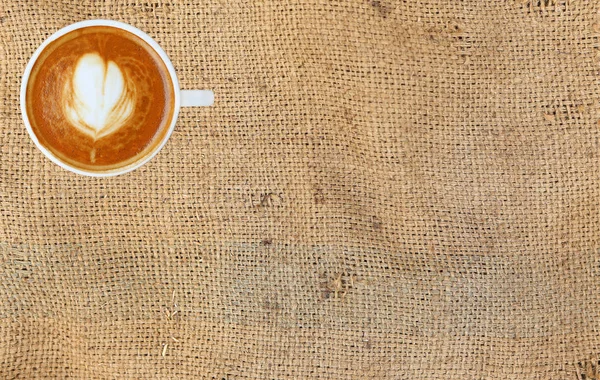 カフェラテ アート スペースとサック背景にハート柄の白いカップとコーヒーのトップ ビュー — ストック写真