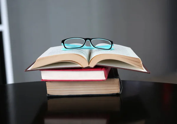 Livro aberto e óculos com pilha de livros de capa dura na mesa de madeira . — Fotografia de Stock