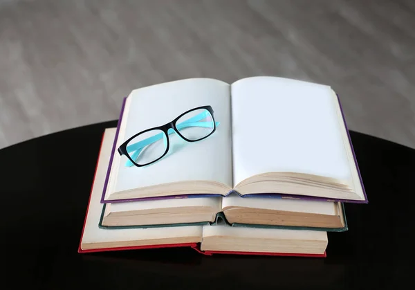 Livro aberto e óculos com pilha de livros de capa dura na mesa de madeira . — Fotografia de Stock