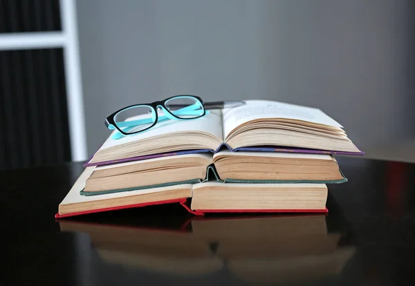 Відкрита книга та окуляри зі стосом книг з твердим покриттям на дерев'яному столі . — стокове фото
