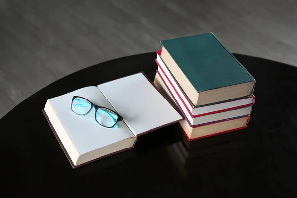 Livro aberto e óculos com pilha de livros de capa dura na mesa de madeira . — Fotografia de Stock