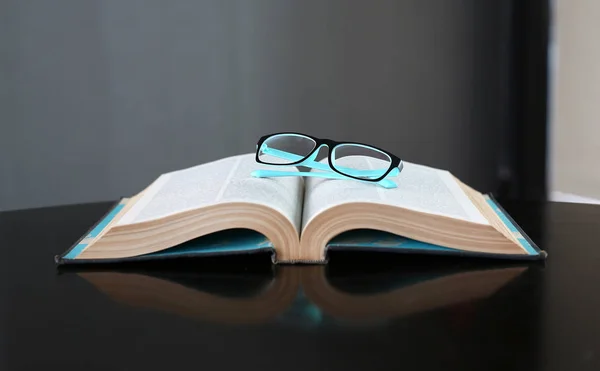 Livro aberto e óculos na mesa de madeira . — Fotografia de Stock