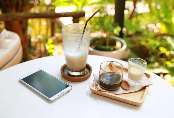 Café caliente y helado con teléfono inteligente en la mesa —  Fotos de Stock