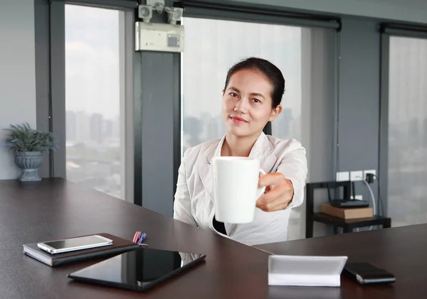 Fiatal üzletasszony ül az asztalnál, a munkahelyi hivatalban kínál egy fehér csésze kávét, összpontosítani az arcát — Stock Fotó