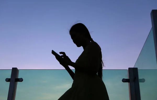 Silhouette of woman using smartphone at sunset on the rooftop of the building — Stock Photo, Image