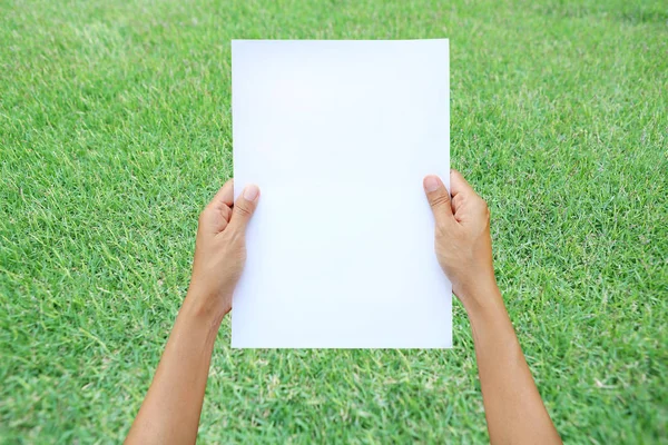 Frau hält Blatt Papier vor grünem Gras-Hintergrund. — Stockfoto