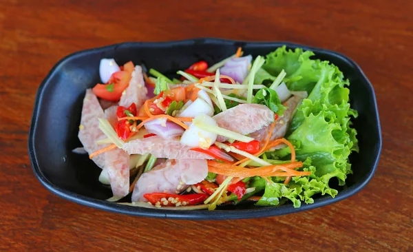 Ensalada de salchicha de cerdo agria tailandesa en plato negro sobre mesa de madera — Foto de Stock