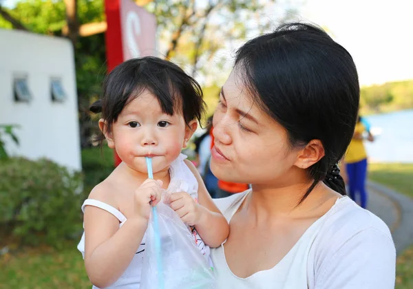 Маленькая азиатка обнимается с матерью в парке, пьет воду через соломинку. — стоковое фото