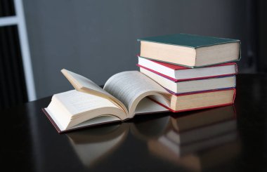 Açık kitap ve ahşap masa üzerinde ciltli kitap yığını.