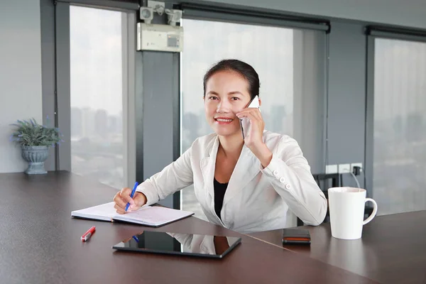 Young businesswoman sitting at the table on workplace in office using the telephone — Stock Photo, Image