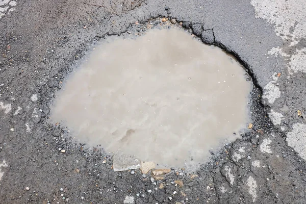 La mauvaise route asphaltée pour les voitures avec un grand nid de poule rempli d'eau — Photo