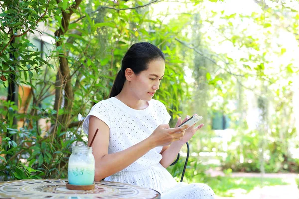 Young asian woman sitting at the gerden and using smart phone — Stock Photo, Image