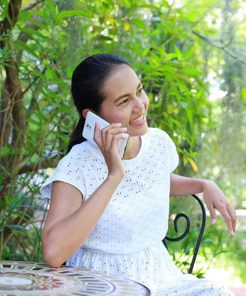 Junge asiatische Frau sitzt im Outdoor-Café und telefoniert — Stockfoto