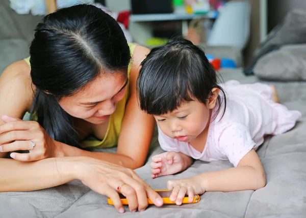 Usia bayi perempuan Asia yang lucu sekitar satu tahun dan delapan bulan bermain smartphone dan berbaring di sofa abu-abu di ruang tamu — Stok Foto