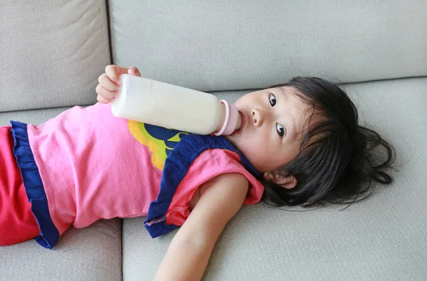 Şirin Asyalı çocuk kız yaşı hakkında bir yaşında ve dokuz aylık kanepe kat mülkiyeti lobide bir şişe içme — Stok fotoğraf