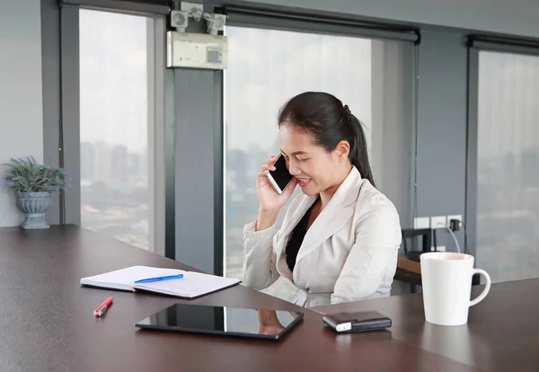 Młoda kobieta siedzi przy stole w miejscu pracy w biurze przy użyciu telefonu — Zdjęcie stockowe