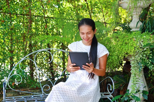 Jonge Aziatische vrouw zitten in de tuin en het gebruik van een tablet — Stockfoto