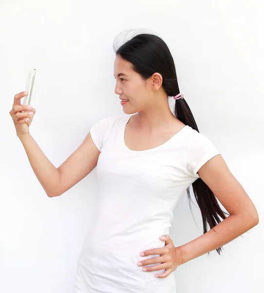 Ung flicka tar bilder på sig själv genom mobilen på vit bakgrund — Stockfoto