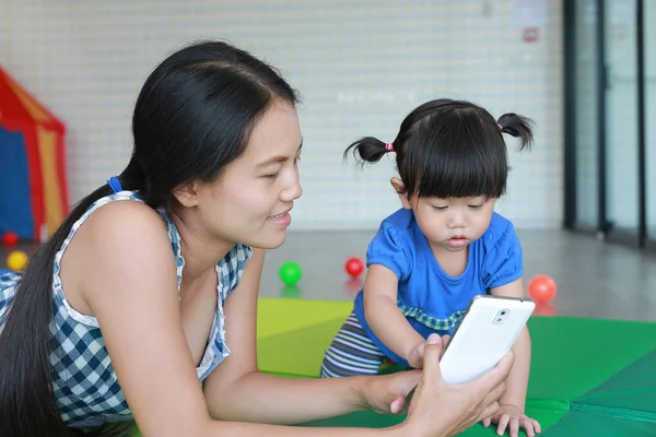 Madre y lindo asiático bebé chica jugando un smartphone y tendido en el Kid habitación — Foto de Stock