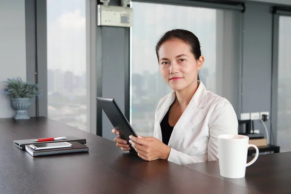 Young businesswoman sitting at the table on workplace in office with playing tablet — Stock Photo, Image