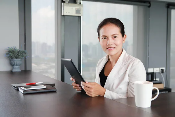 Young businesswoman sitting at the table on workplace in office with playing tablet — Stock Photo, Image