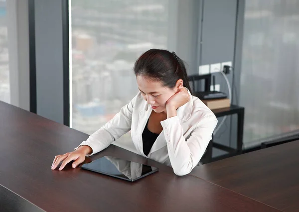 Young businesswoman sitting at the table on workplace in office with playing tablet — Stock Photo, Image