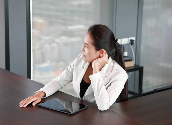 Junge Geschäftsfrau sitzt am Tisch am Arbeitsplatz im Büro mit Tablet und schaut raus — Stockfoto