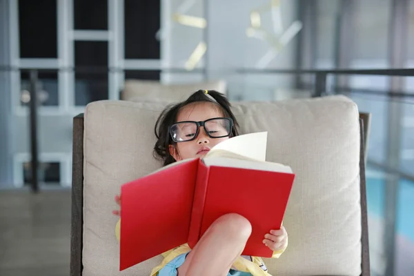 Kind meisje met bril lezen boek in bibliotheek, onderwijs concept. — Stockfoto