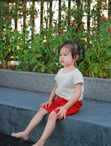 Bonito pouco ásia menina sentado no pedra banco no o jardim . — Fotografia de Stock