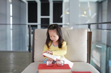 Küçük çocuk kız okuma kitabı kitaplığında, eğitim kavramı.