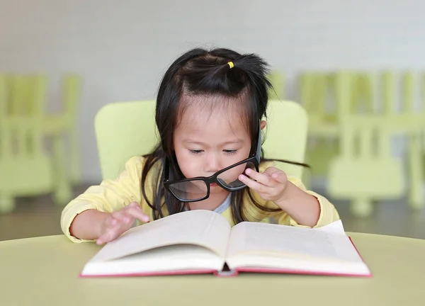 Έξυπνο μικρό παιδί κορίτσι φορώντας γυαλιά διαβάζοντας ένα βιβλίο για το παιδικό δωμάτιο. — Φωτογραφία Αρχείου