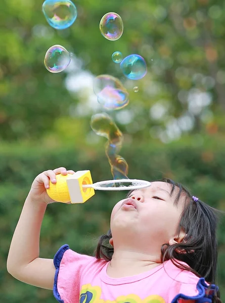 Азиатская маленькая девочка надувает мыльные пузыри в зеленом парке — стоковое фото