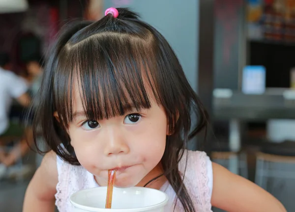 Ładna dziewczynka przy użyciu słomy pić spadzi z plastikowy kubek w kawiarni — Zdjęcie stockowe