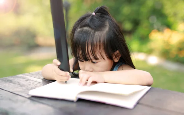 Meisje kind schrijven op tafel in de tuin, onderwijs concept. — Stockfoto