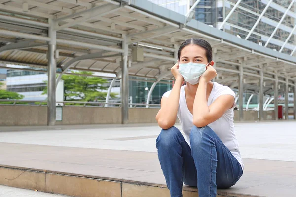 Kvinna som bär skyddande mask för att skydda föroreningar och influensa sitter vid offentliga området. — Stockfoto