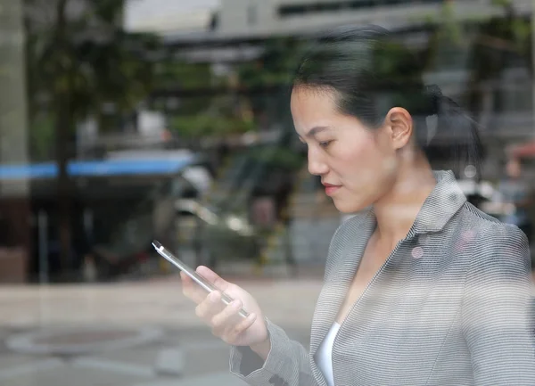 Beautiful business woman using a smartphone at reflection glass of office building. — Stock Photo, Image