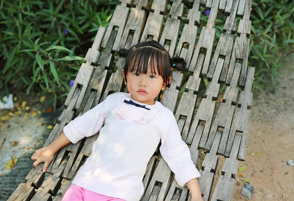 Little girl lying on wood cradle in a garden — Stock Photo, Image