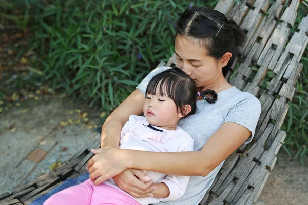 Moeder en kind meisje liggend op houten wieg in een tuin — Stockfoto