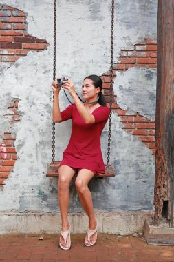 Fotoğraf makinesi alarak ve salıncak eski tuğla duvar arka plan üzerinde oturan Asyalı kadın