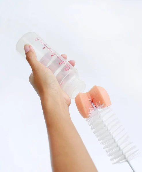 Рука матери мыть бутылочку молока с помощью бутылочки щетки на белом фоне — стоковое фото