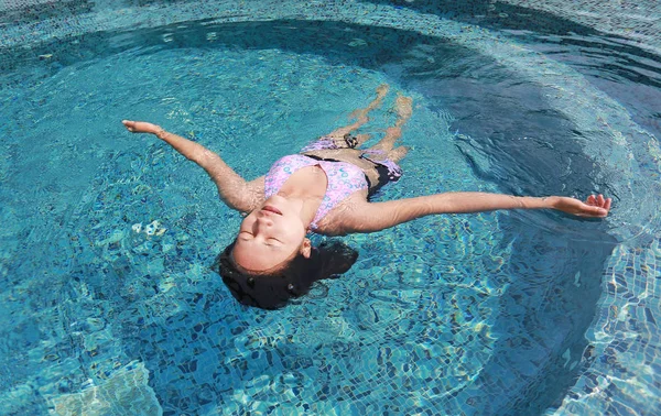 Młoda kobieta unosi się na powierzchni wody z basenu — Zdjęcie stockowe