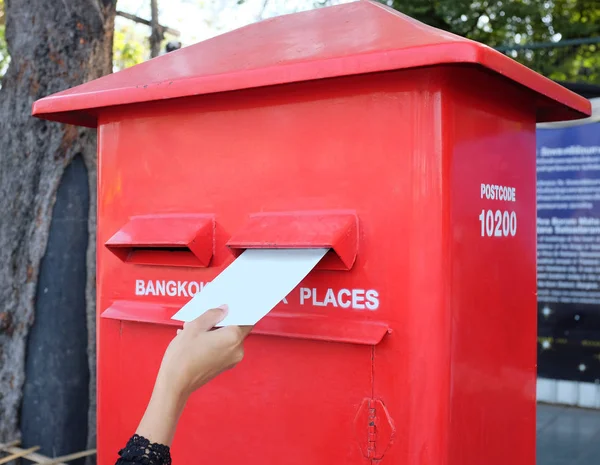 Hand sending a letter or postcard in a red Postbox.