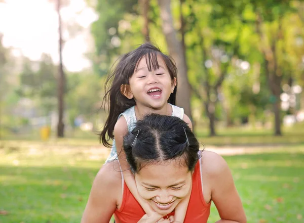 Gelukkig meisje op de achterkant van haar moeder in de tuin — Stockfoto