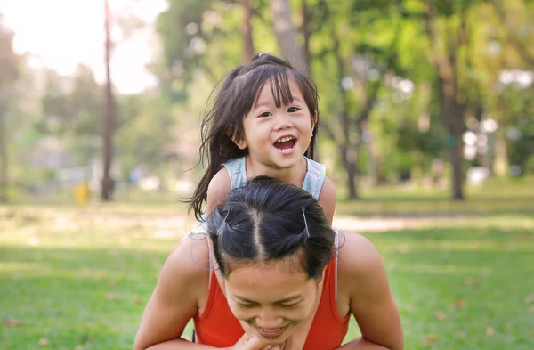 Glückliches kleines Mädchen auf dem Rücken ihrer Mutter im Garten — Stockfoto